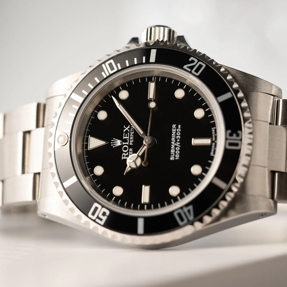 Detailaufnahme der seitlich auf dem Uhrengehäuse liegenden Rolex Submariner No Date 14060M mit schwarzem Zifferblatt und der klassischen schwarzen Aluminium-Lünette