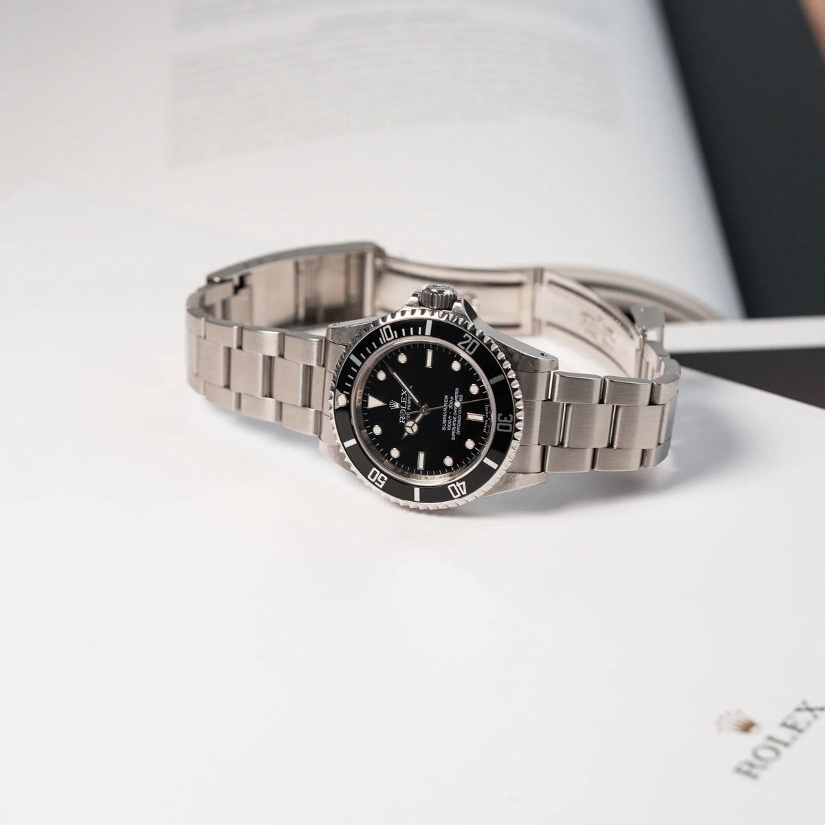 Rolex Submariner NoDate 14060M in Schwarz liegt auf einem Rolex-Buch