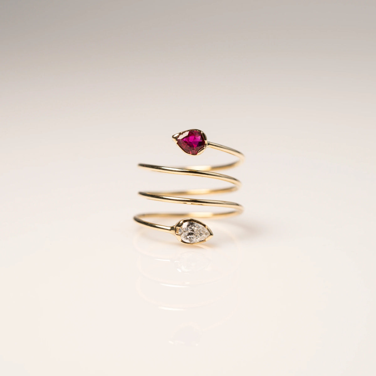 Produktfotografie des Gelbgoldrings "Twisted Drop" aus der Schmuckatelier Lang Collection, der an eine Spirale erinnert und als Blickfang zum Abschluss der offenen Ringschiene einen Rubin und einen funkelnden Brillanten in Tropfenform verbaut hat