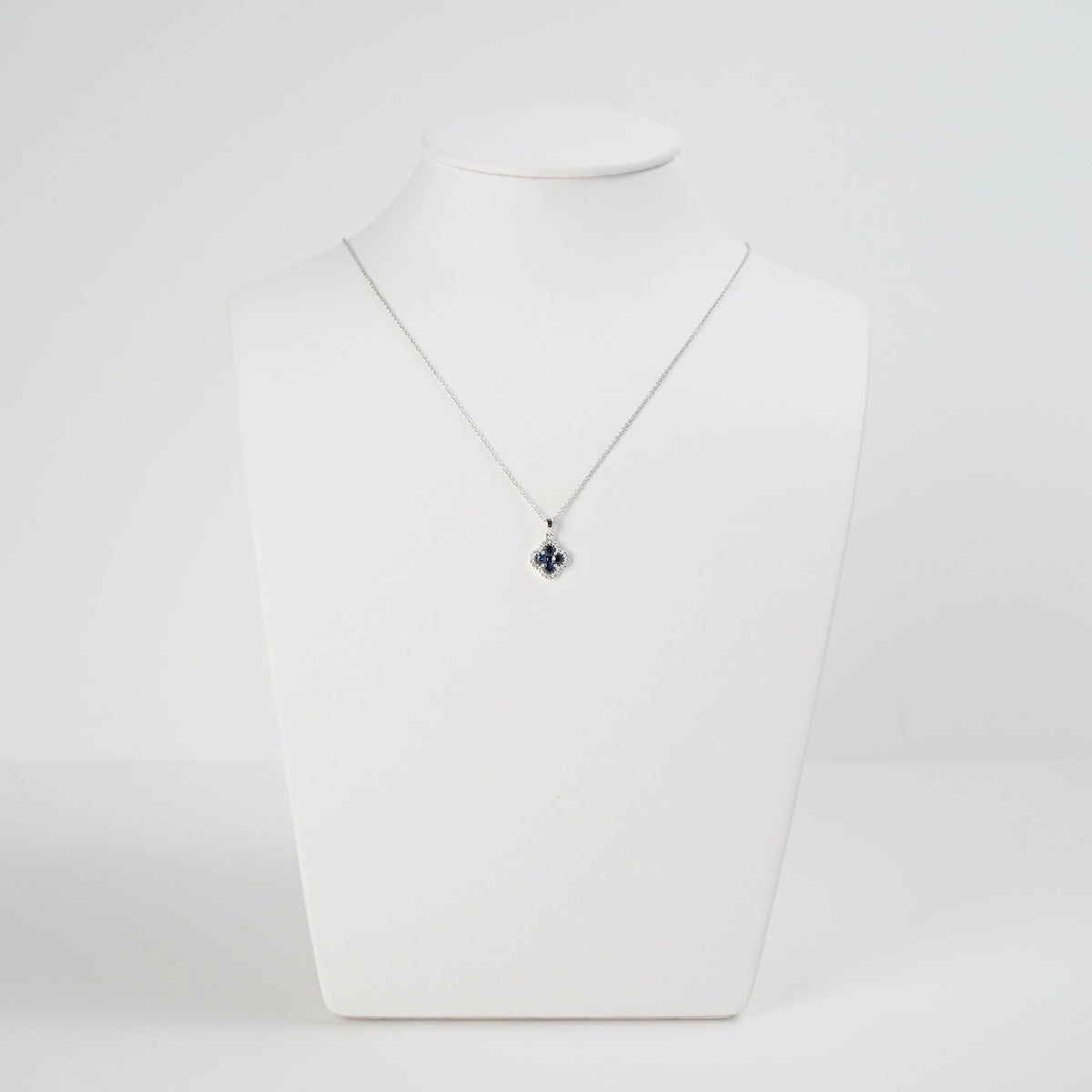 Saphir Kleeblatt Kette aus Weißgold mit einem Saphir-Brillant-Anhänger in einer Kleeblatt-Form, bei dem die Saphire durch die kleinen Diamanten umrandet sind, wird auf einer Schmuckbüste präsentiert
