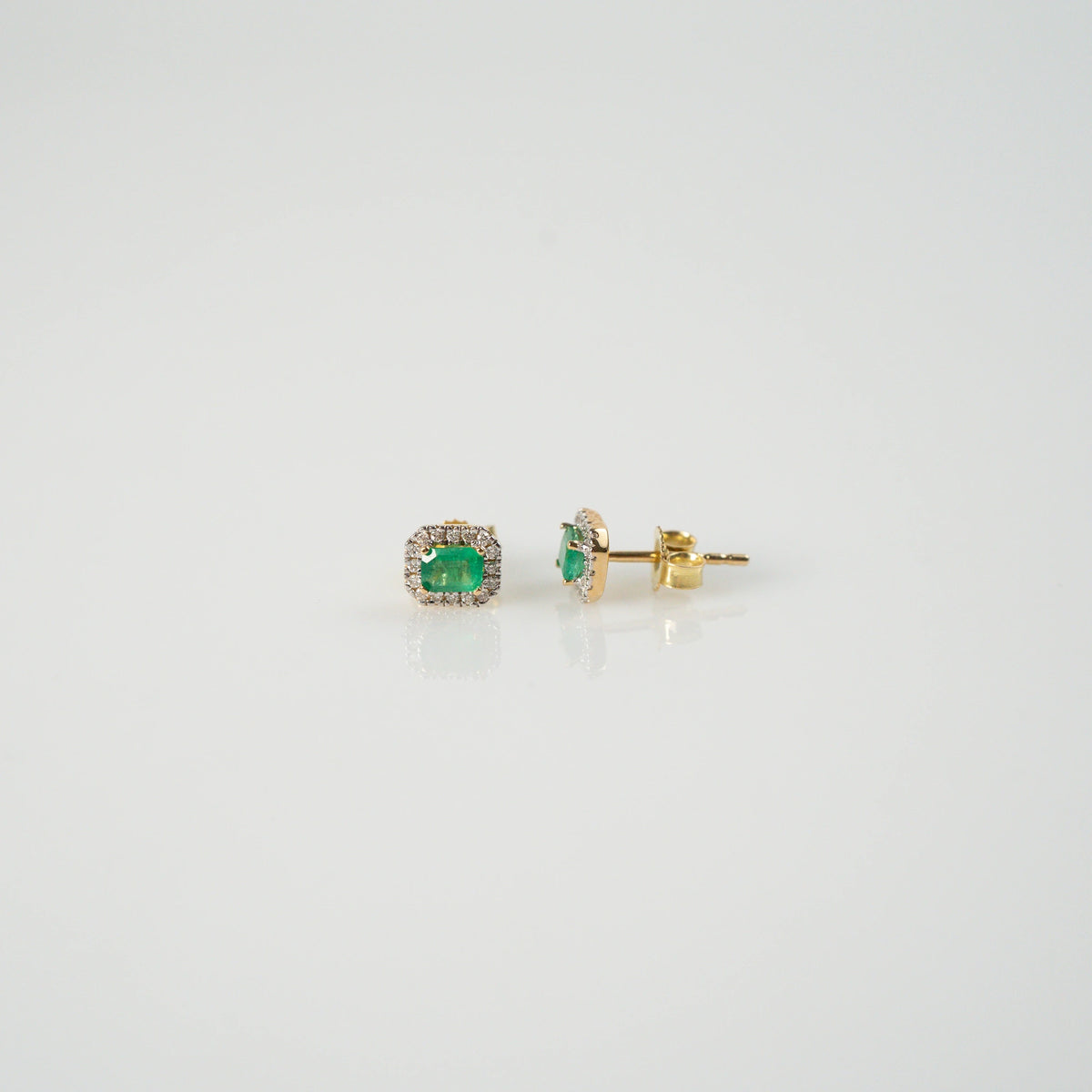 Produktfotografie mit zentralem und seitlichem Blick auf die jeweils aus Gelbgold gefertigten Smaragd-Brillant-Ohrstecker aus der Schmuckatelier Lang Collection, bei denen der zentrale, kräftig grüne Smaragd durch einen Diamantkranz eingerahmt ist