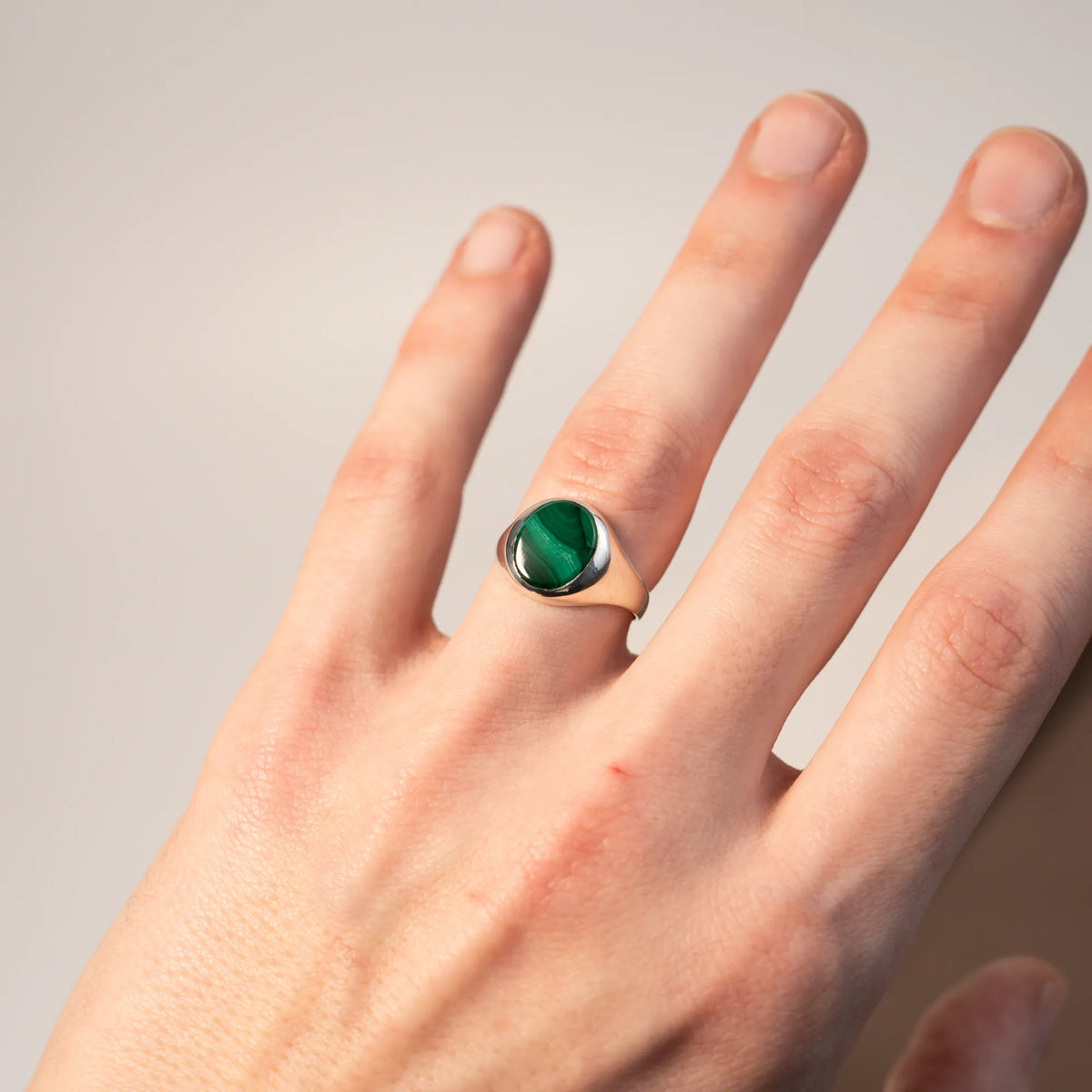 Mann präsentiert den handgefertigten Siegelring aus 925er Silber mit einem eingefassten, ovalen Malachit Edelstein an seinem Ringfinger in die Kamera