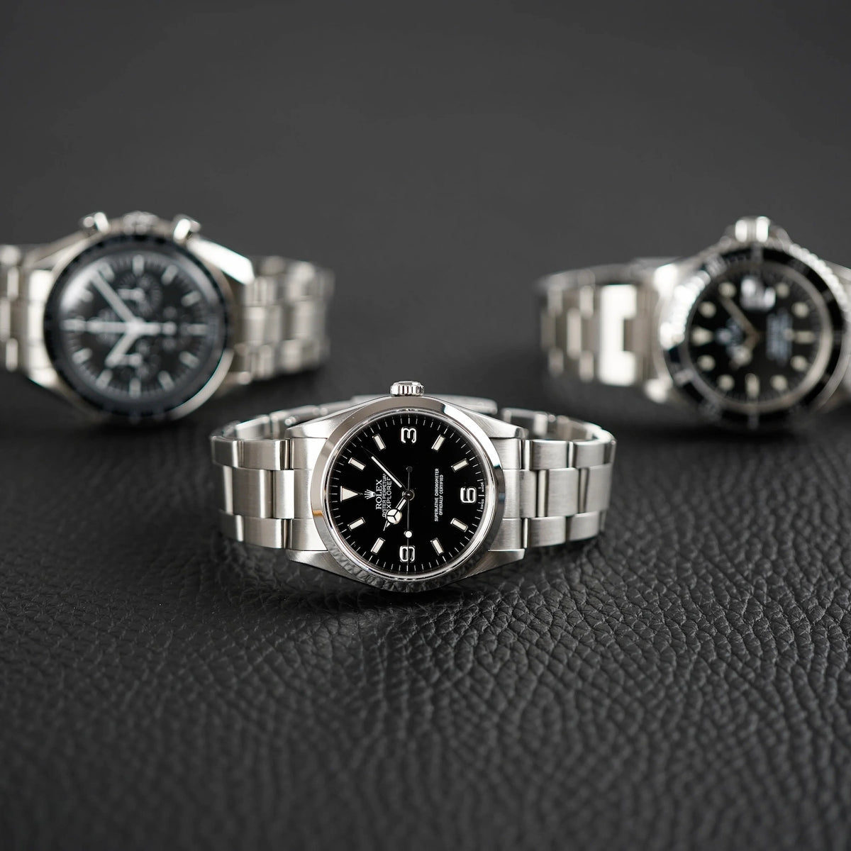 Exklusive Luxusuhren von Rolex und Omega liegen auf schwarzer Ledermatte