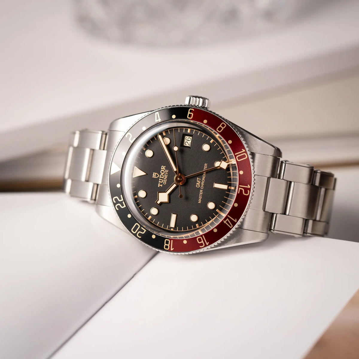 Produktfotografie der seitlich auf dem Uhrengehäuse liegenden Tudor BlackBay GMT Coke der Referenz 7939G1A0NRU mit der schwarz-roten Lünette und bronzefarbenen Details am Edelstahlarmband