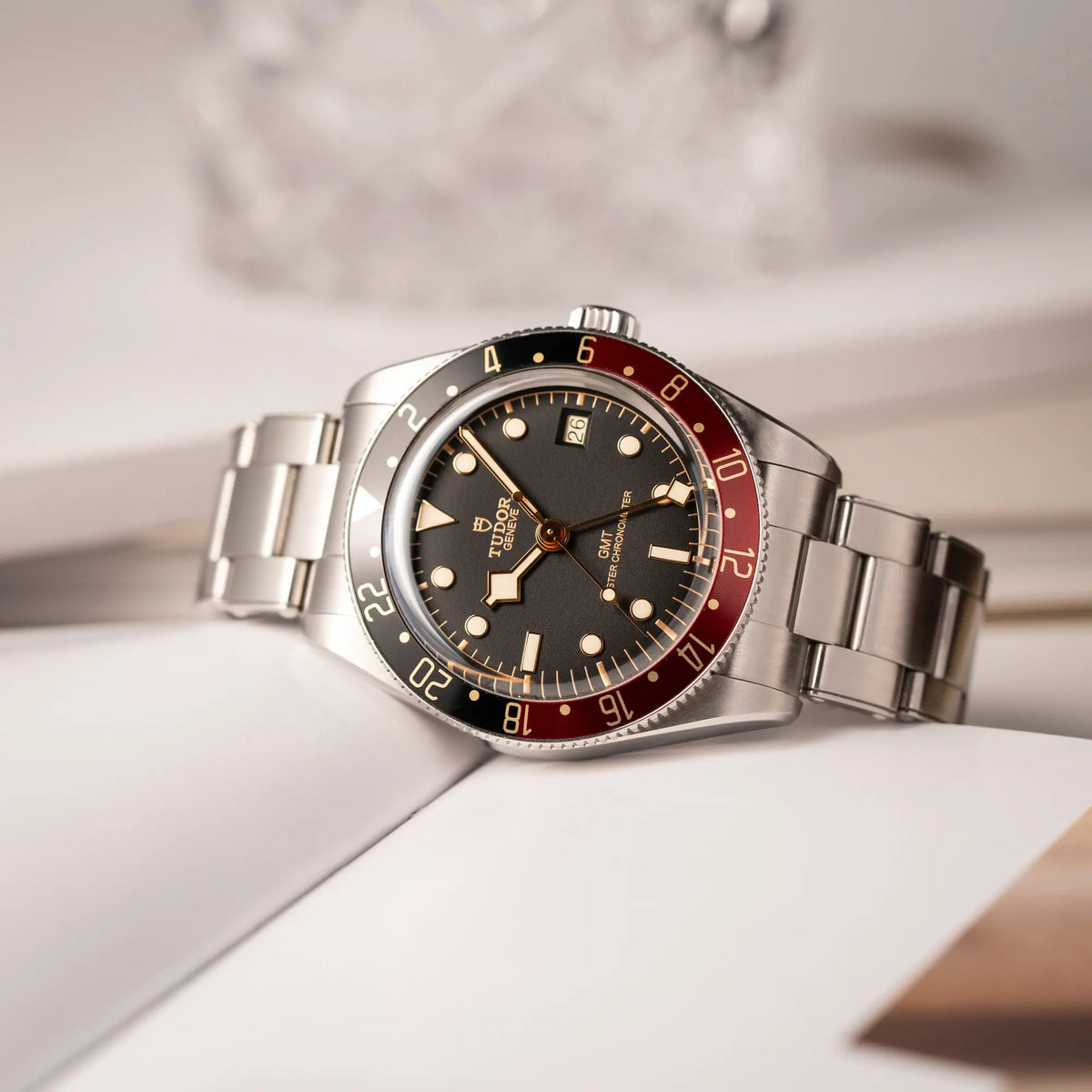 Tudor BlackBay GMT Coke der Referenz 7939G1A0NRU mit der schwarz-roten Lünette und bronzefarbenen Details am Edelstahlarmband liegt schräg auf einem Uhrenbuch