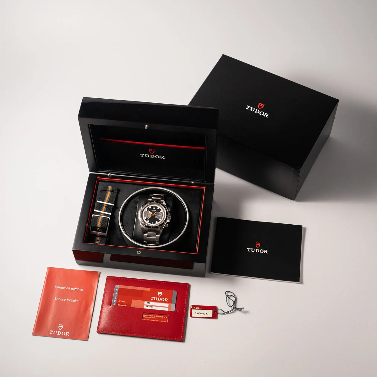 Lieferumfang zu dem Tudor Black Bay Heritage Chronograph der Referenz 70330N mit schwarzem Zifferblatt und orangen Details, bestehend aus Box mit Umkarton, Hangtag, Booklets und originaler Garantiekarte und zusatzlichem Nato-Band