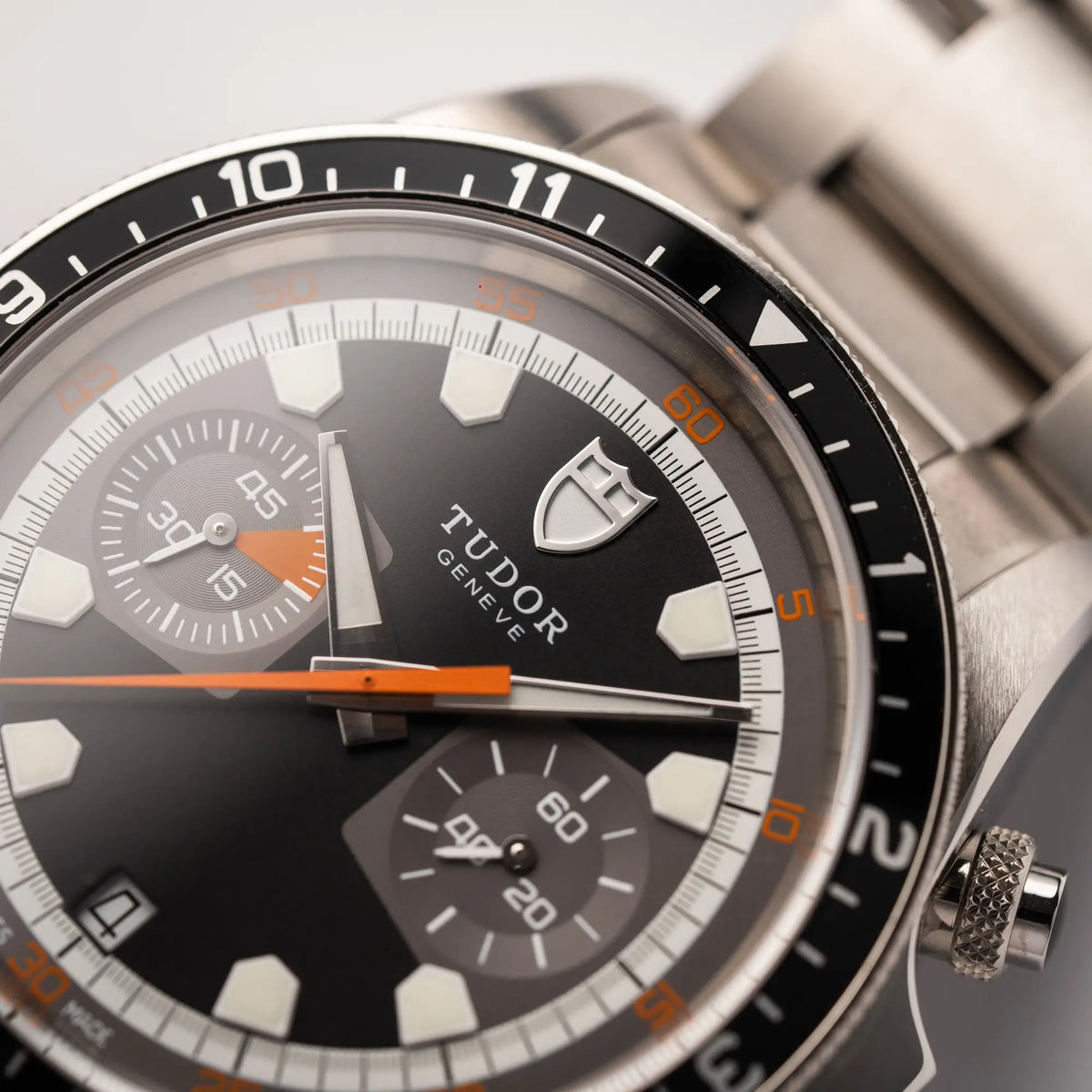 Detailaufnahme des Tudor Logos bei 12 Uhr von dem Tudor Black Bay Heritage Chronograph der Referenz 70330N mit schwarzem Zifferblatt und orangen Details