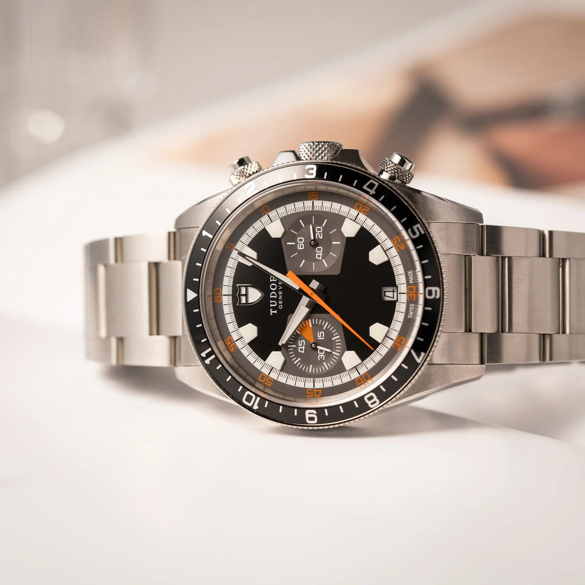 Produktfotografie con der seitlich liegenden Tudor Black Bay Heritage Chronograph der Referenz 70330N mit schwarzem Zifferblatt und orangen Details
