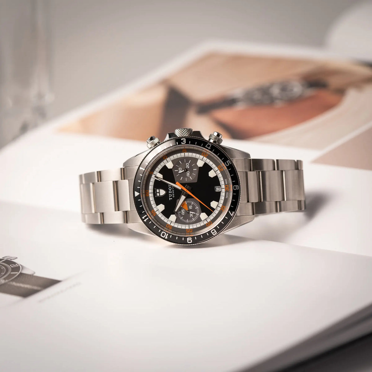Tudor Black Bay Heritage Chronograph der Referenz 70330N mit schwarzem Zifferblatt und orangen Details liegt seitlich auf einem Uhrenmagazin