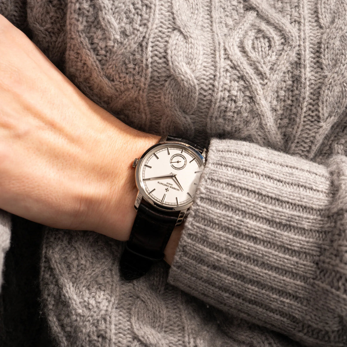 Mann in einem grauen Strickpullover trägt die Vacheron Constantin Traditionelle 82172 mit weißem Zifferblatt und einem Weißgold-Gehäuse am braunem Lederband an seinem Handgelenk