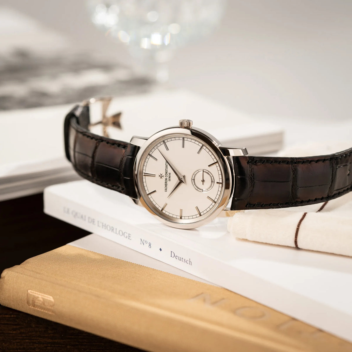 Produktfotografie der seitlich auf dem Gehäuse liegenden Vacheron Constantin Traditionelle 82172 mit weißem Zifferblatt und einem Weißgold-Gehäuse am braunem Lederband