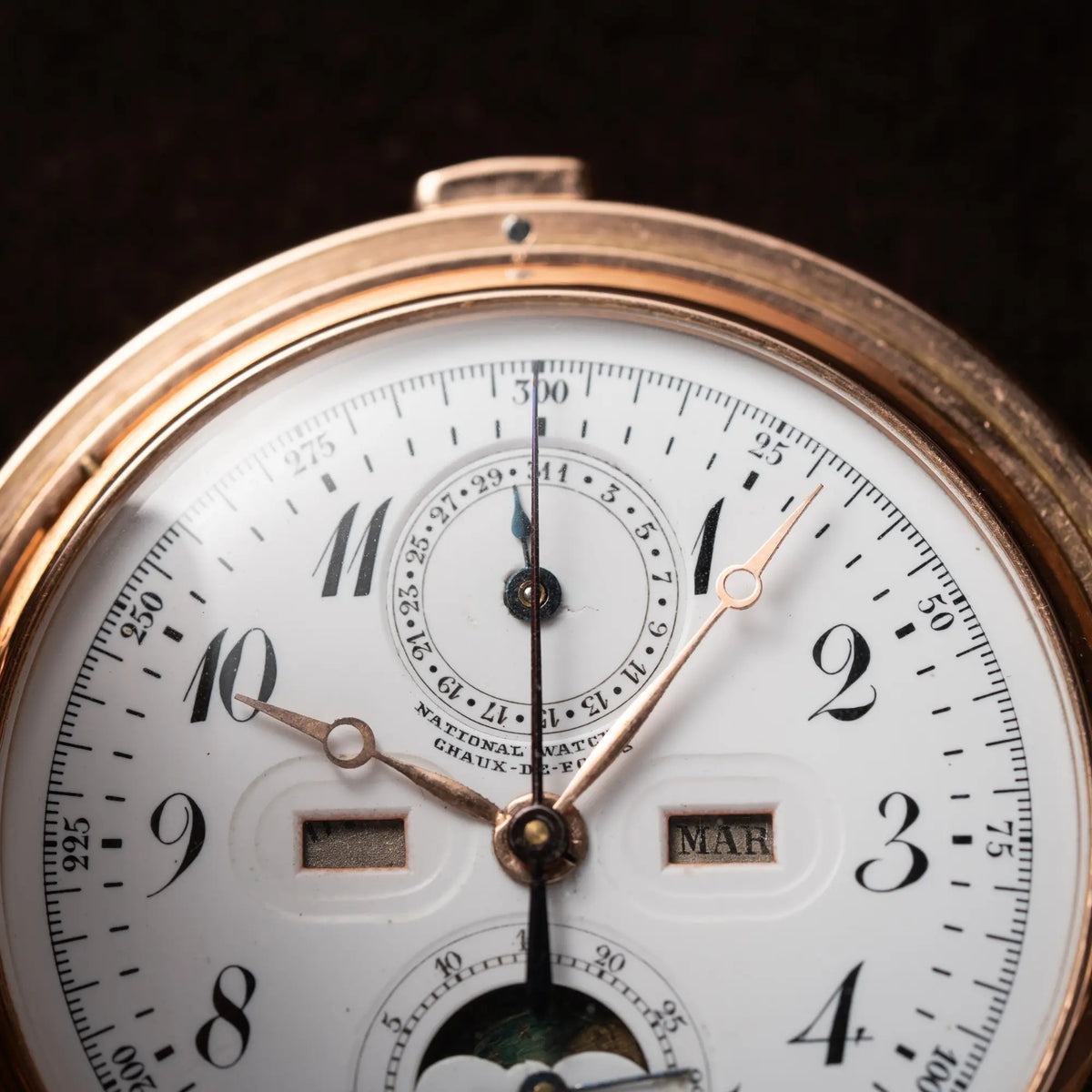 Detailaufnahme des Zeigersatzes von der Vollkalender Taschenuhr aus 14 Karat Roségold mit viertel Stunden Repetition und Mondphase-Anzeige bei 6 Uhr