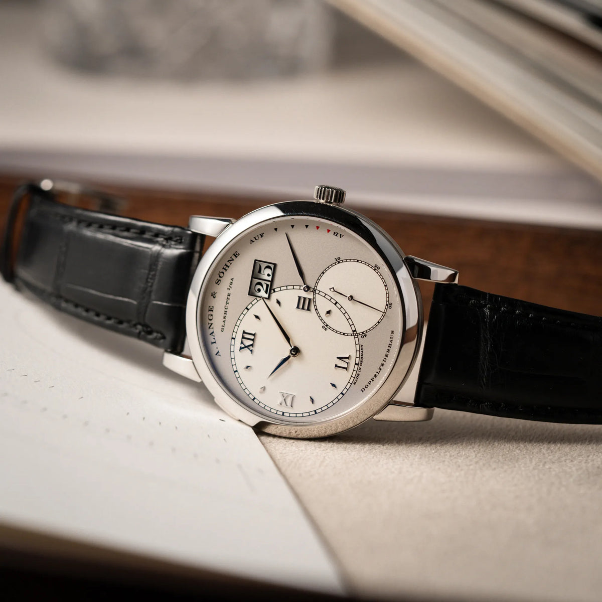 Produktfotografie der Großen Lange 1 mit Platingehäuse und silberfarbenem Zifferblatt am schwarzen Lederband von A. Lange & Söhne, während die Uhr auf Juwelierstablet liegt