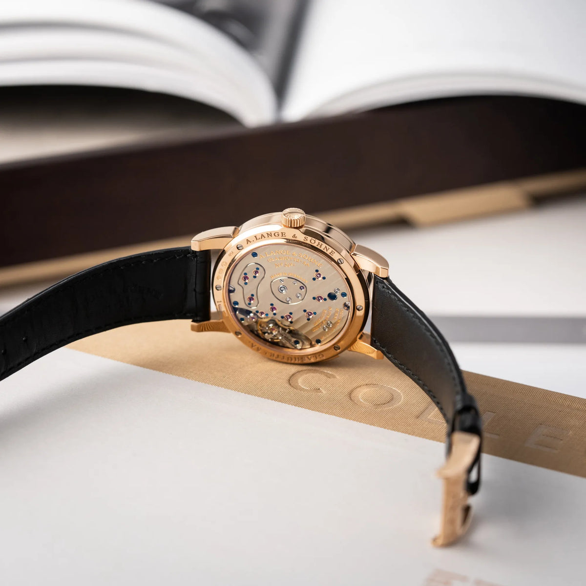 Produktfotografie der A. Lange & Söhne Lange 1 der Referenz 101.032 mit 38,5mm-Roségold-Gehäuse und dem für das Modell typische, asymmetrisch angeordnete Zifferblatt mit Großdatum zeigt die geöffnete Dornschliesse und  das Caliber L901.0 durch den Glasboden