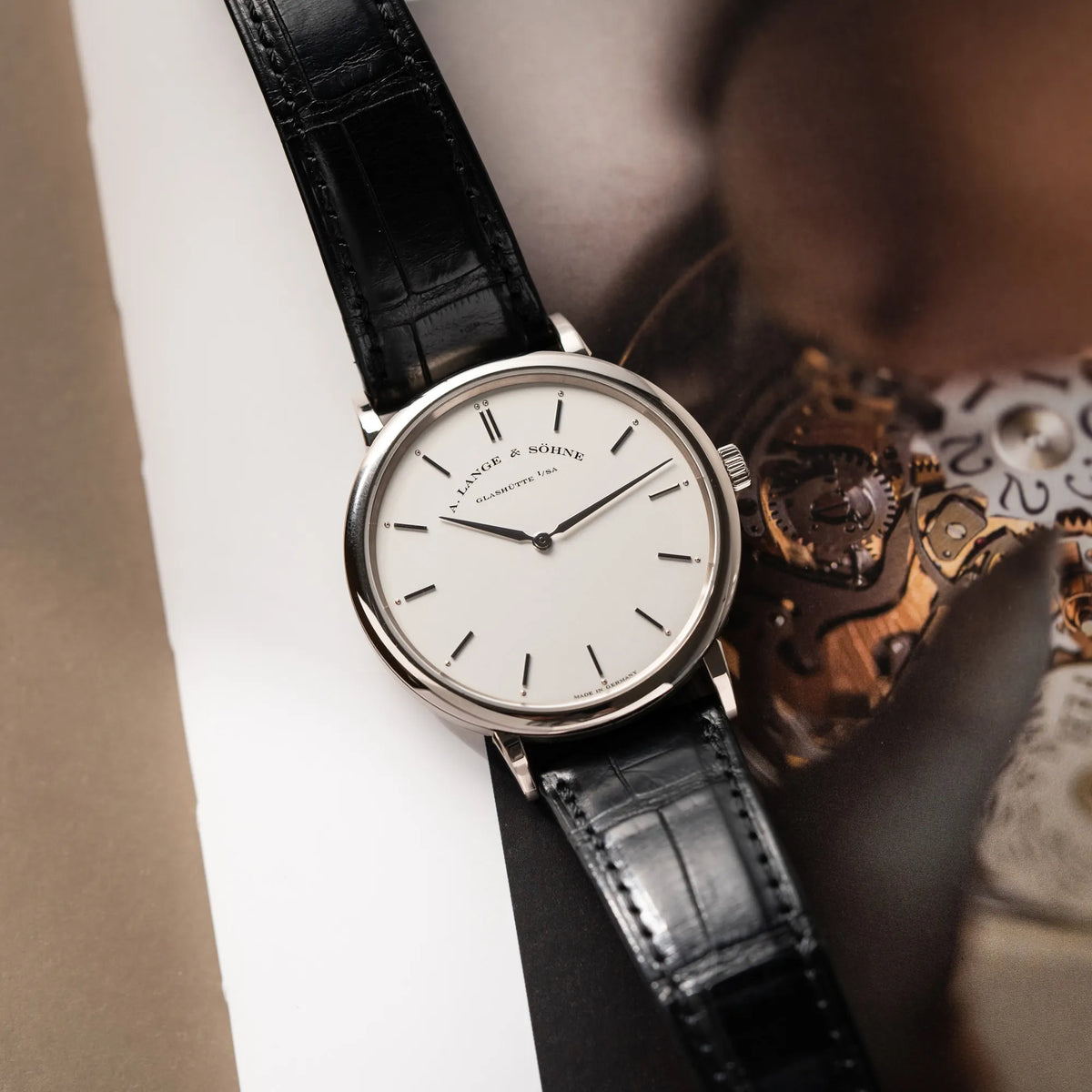 A.Lange Söhne Saxonia Thin der Referenz 211.026 im Weißgold-Gehäuse mit weiß-silbernem Zifferblatt am schwarzen Lederarmband liegt auf einem Uhrenbuch