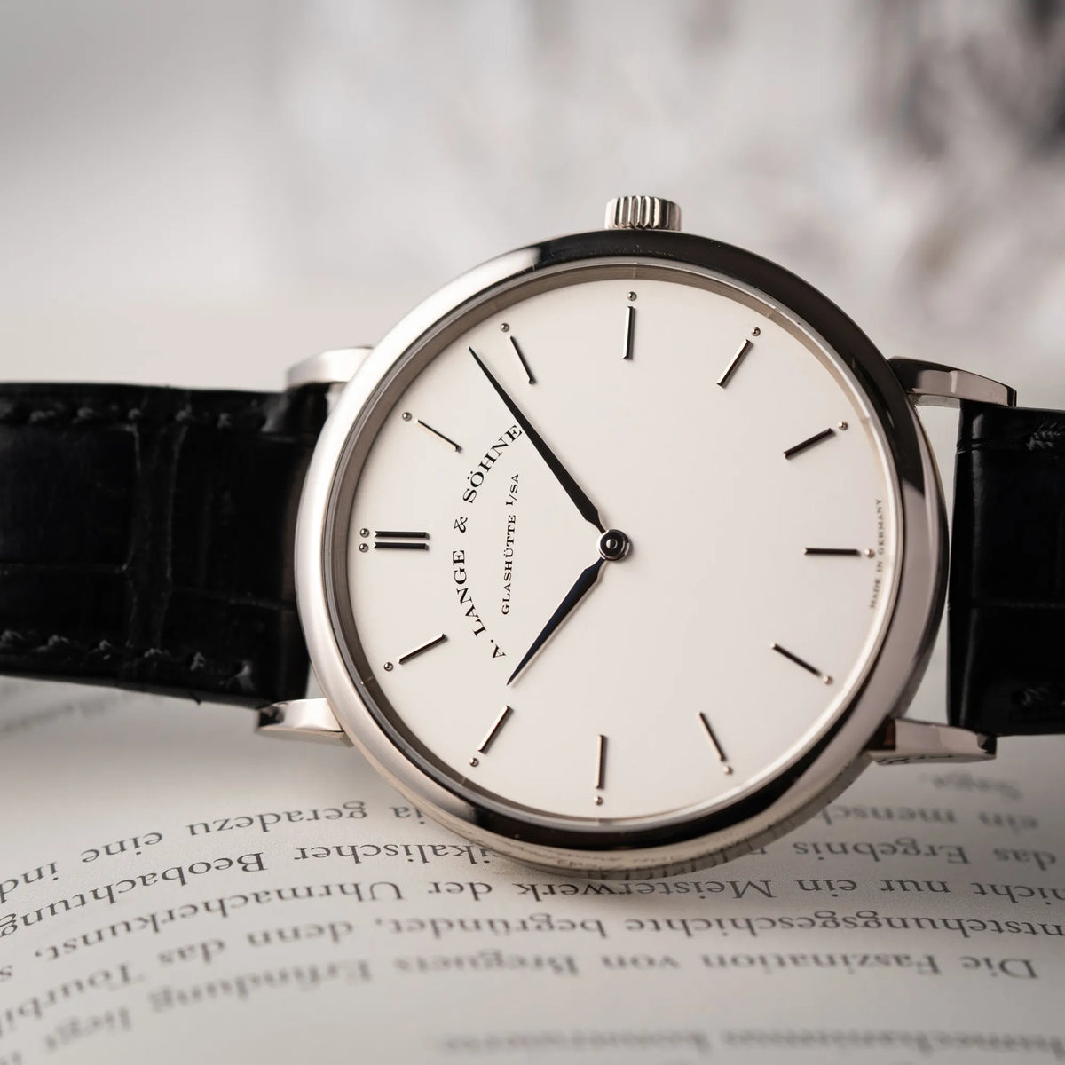 Detailaufnahme der seitlich auf dem Uhrengehäuse liegenden A.Lange Söhne Saxonia Thin der Referenz 211.026 im Weißgold-Gehäuse mit weiß-silbernem Zifferblatt am schwarzen Lederarmband