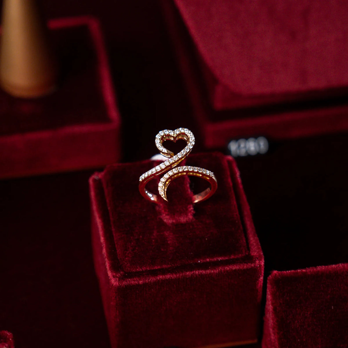 Produktfotografie des in Gelbgold gefertigten Damenrings mit geschwungener Ringschiene und Herzform und Diamantbesatz, während der Ring auf einem weinroten, samtigen Ständer präsentiert wird