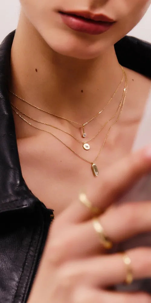 Frau trägt verschieden Schmuckstücke (Halsketten und Ringe) von Alisia Jewels, die aus vergoldetem Silber gefertigt werden