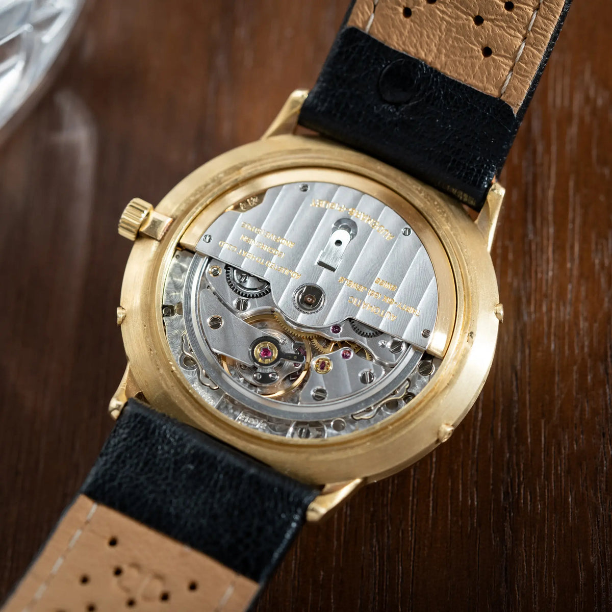 Blick auf das automatische Uhrwerk durch den geöffneten Gehäuseboden der Audemars Piguet Quantième Perpétual der Referenz 5548BA mit 36mm-Gelbgold-Gehäuse und weißem Zifferblatt an einem schwarzen Lederband