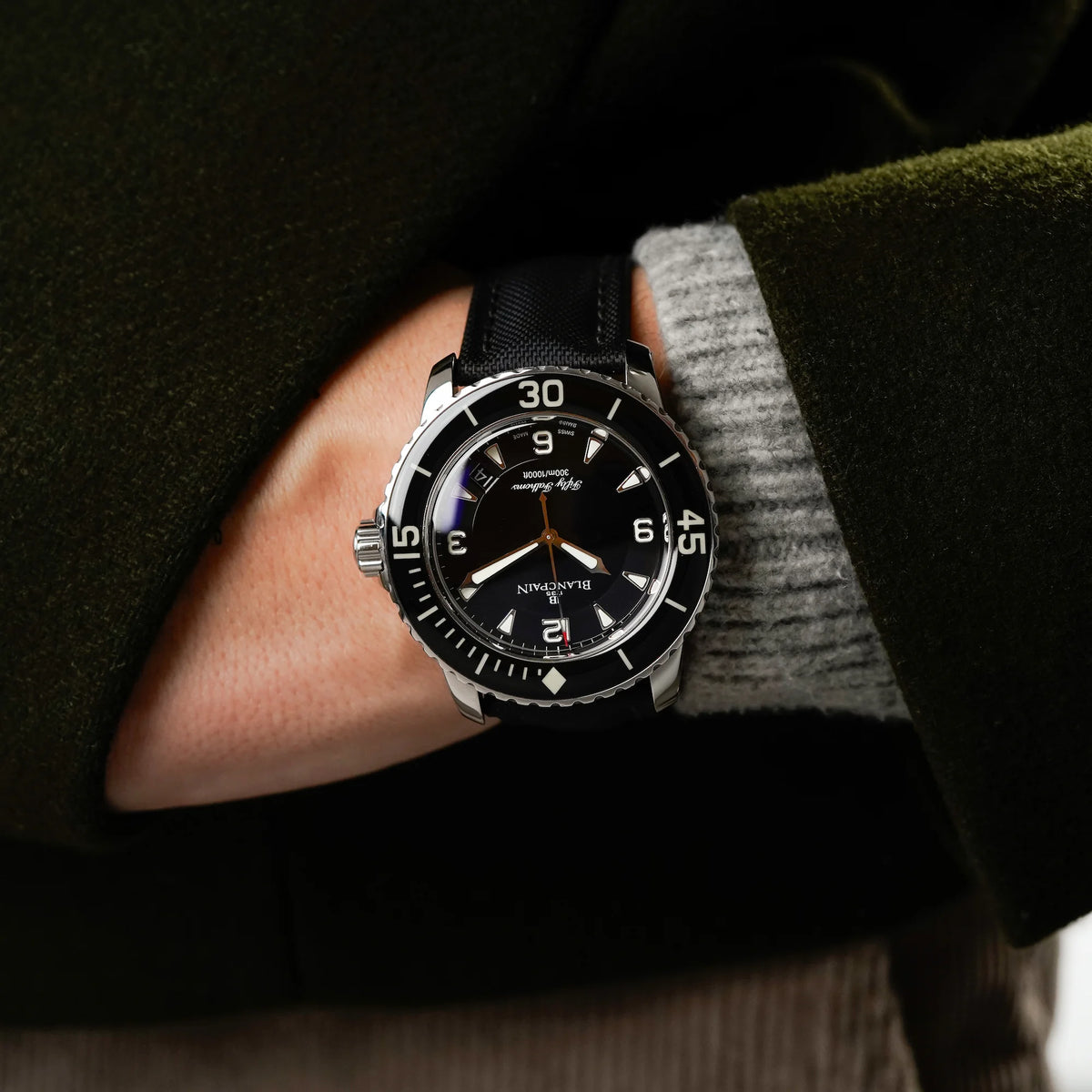 Mann trägt die Blancpain Fifty Fathoms in Schwarz am Nylon-Band an seinem Handgelenk, während seine Hand in seiner Jackentasche steckt