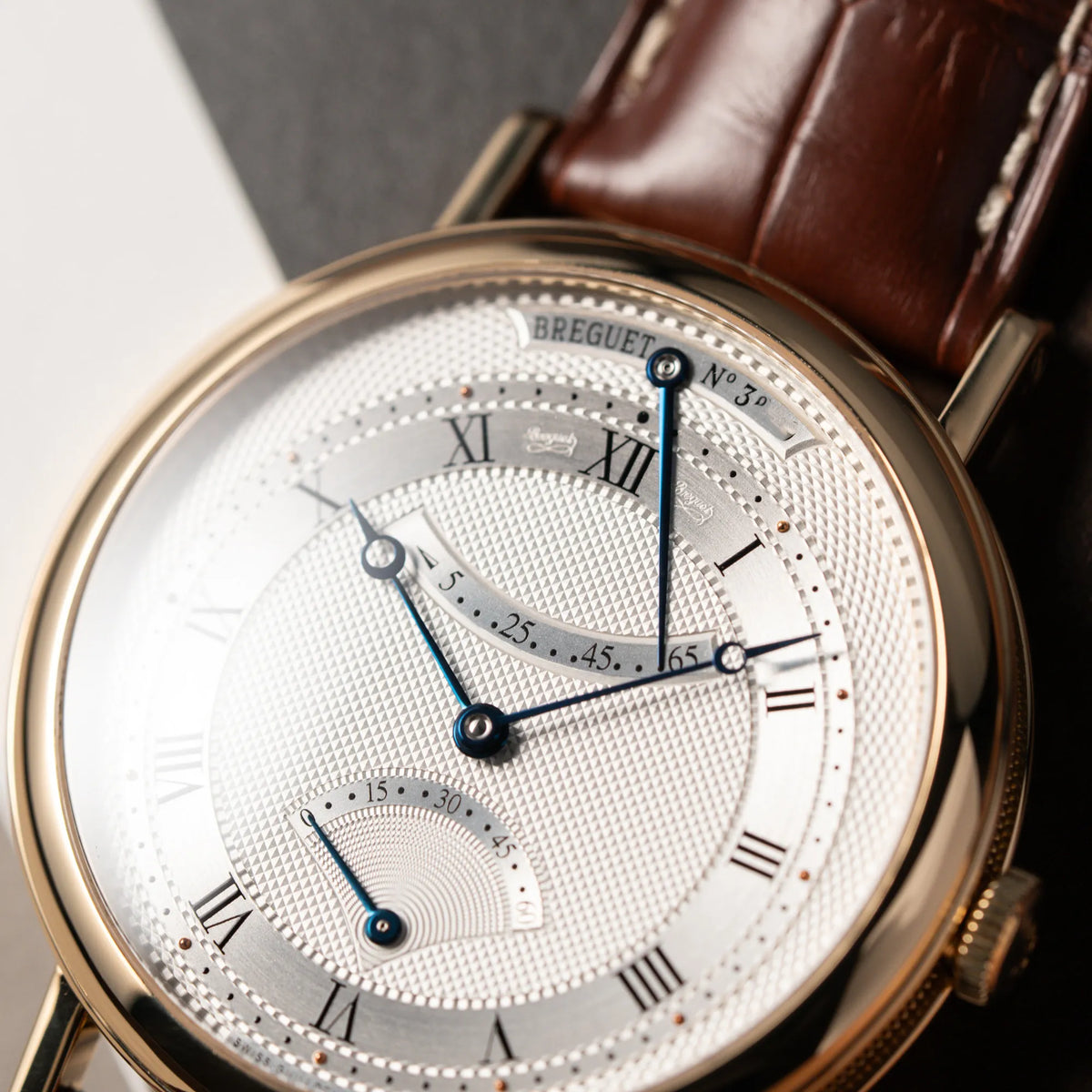 Detailaufnahme des Zifferblatts der der gelbgoldenen Breguet Armbanduhr des Models Classic Retrograde 5207 am braunen Lederband