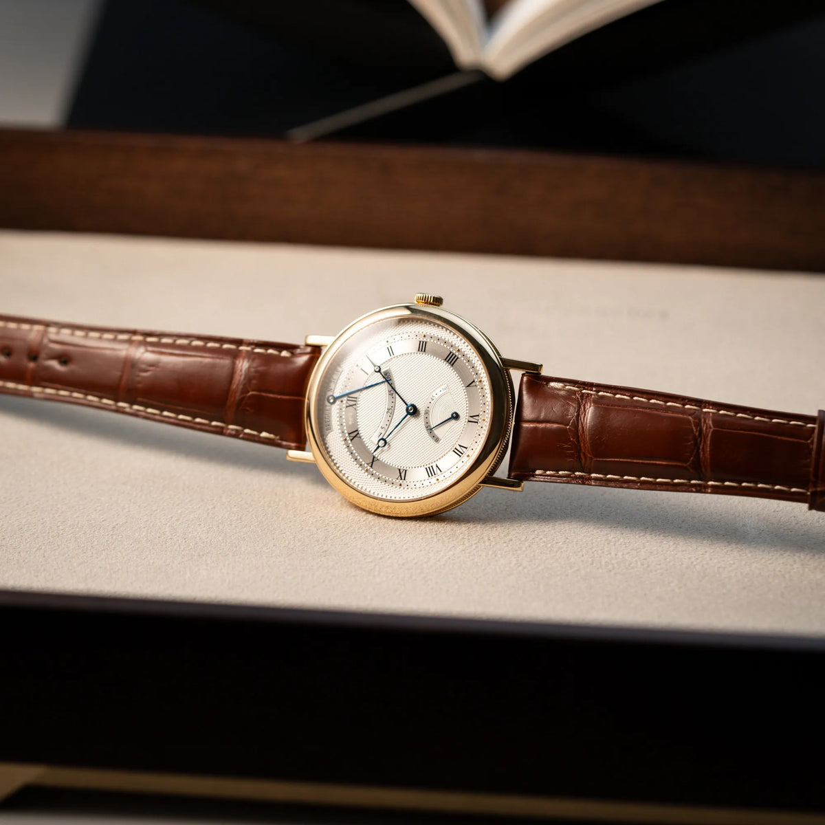 Produktfotografie der seitlich liegenden, gelbgoldenen Breguet Armbanduhr des Models Classic Retrograde 5207 am braunen Lederband