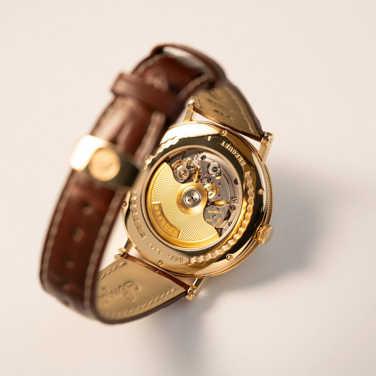 Gehäuseboden der gelbgoldenen Breguet Armbanduhr des Models Classic Retrograde 5207 am braunen Lederband mit Sichtglas für einen Blick auf das mechanische Uhrwerk