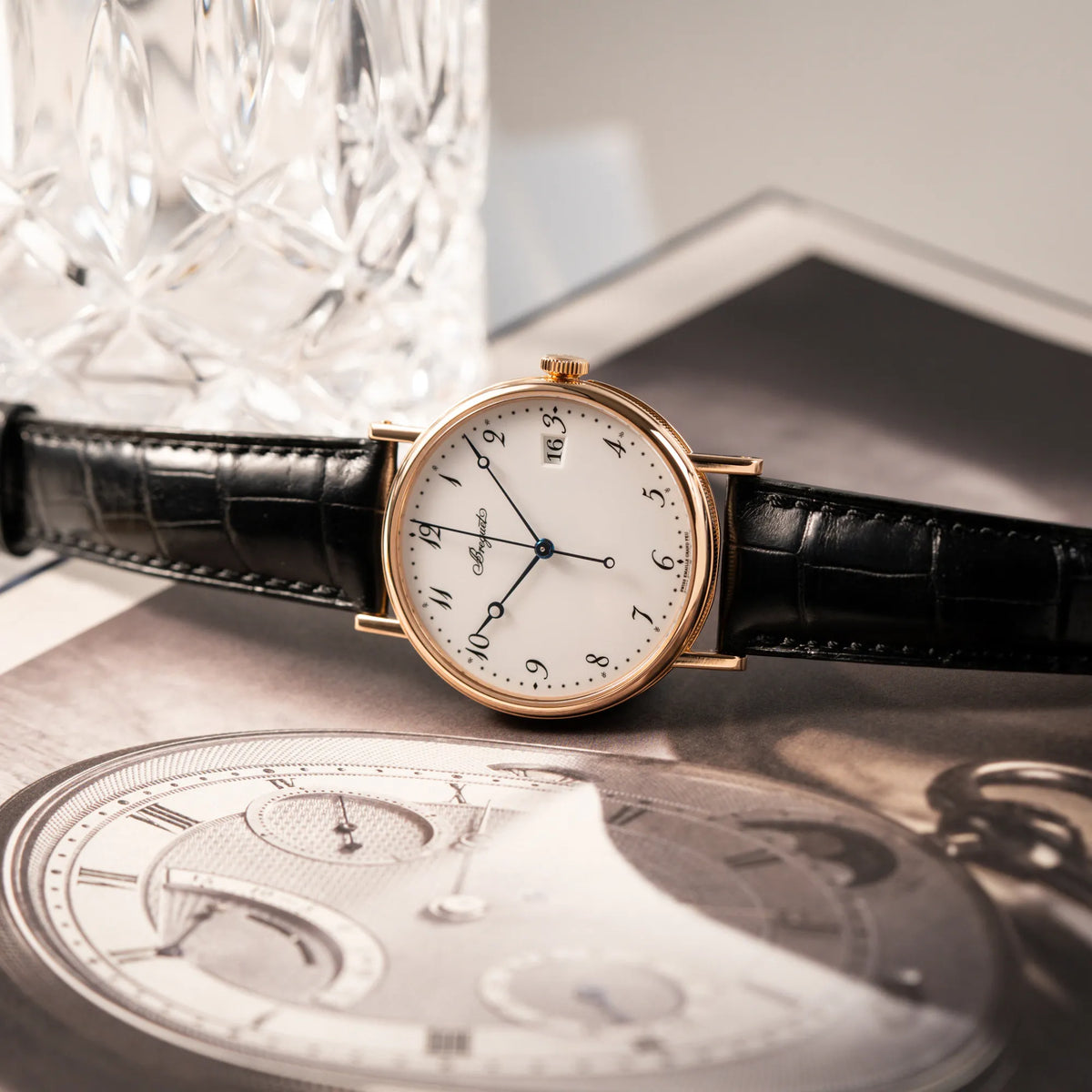 Produktfotografie der seitlich auf dem Gehäuse liegenden Breguet Classique 5177 in Roségold mit weißem Emaille-Zifferblatt
