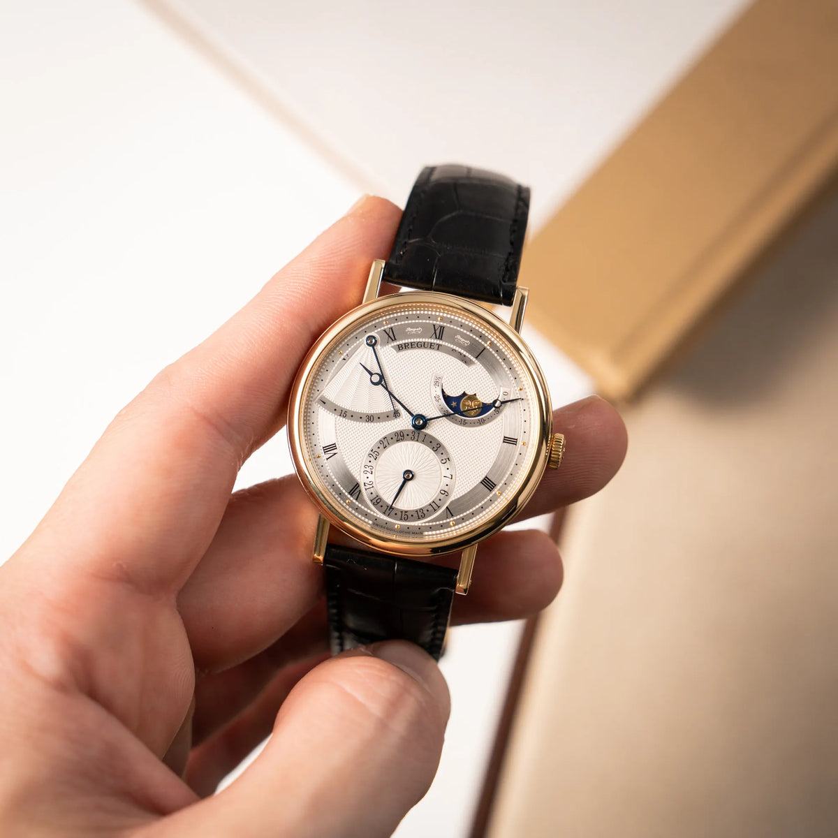 Mann hält die Breguet Classique 7137BA mit einem Gelbgoldgehäuse in klassischer Form mit einem silbernen Zifferblatt mit jeweils einem anderen handgefertigten Guilloche-Muster für jede Komplikation  in seiner Hand und präsentiert die Uhr in die Kamera