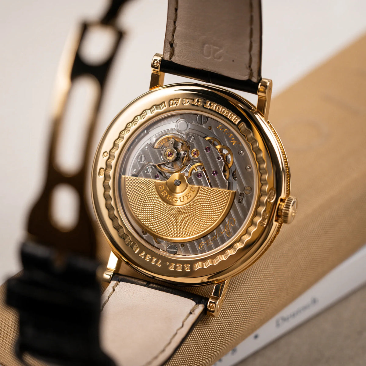 Produktfotografie zeigt Micro-Rotor und das Automatik-Uhrwerk durch den Sichtboden der Breguet Classique 7137BA mit einem Gelbgoldgehäuse in klassischer Form mit einem silbernen Zifferblatt mit jeweils einem anderen handgefertigten Guilloche-Muster für jede Komplikation 
