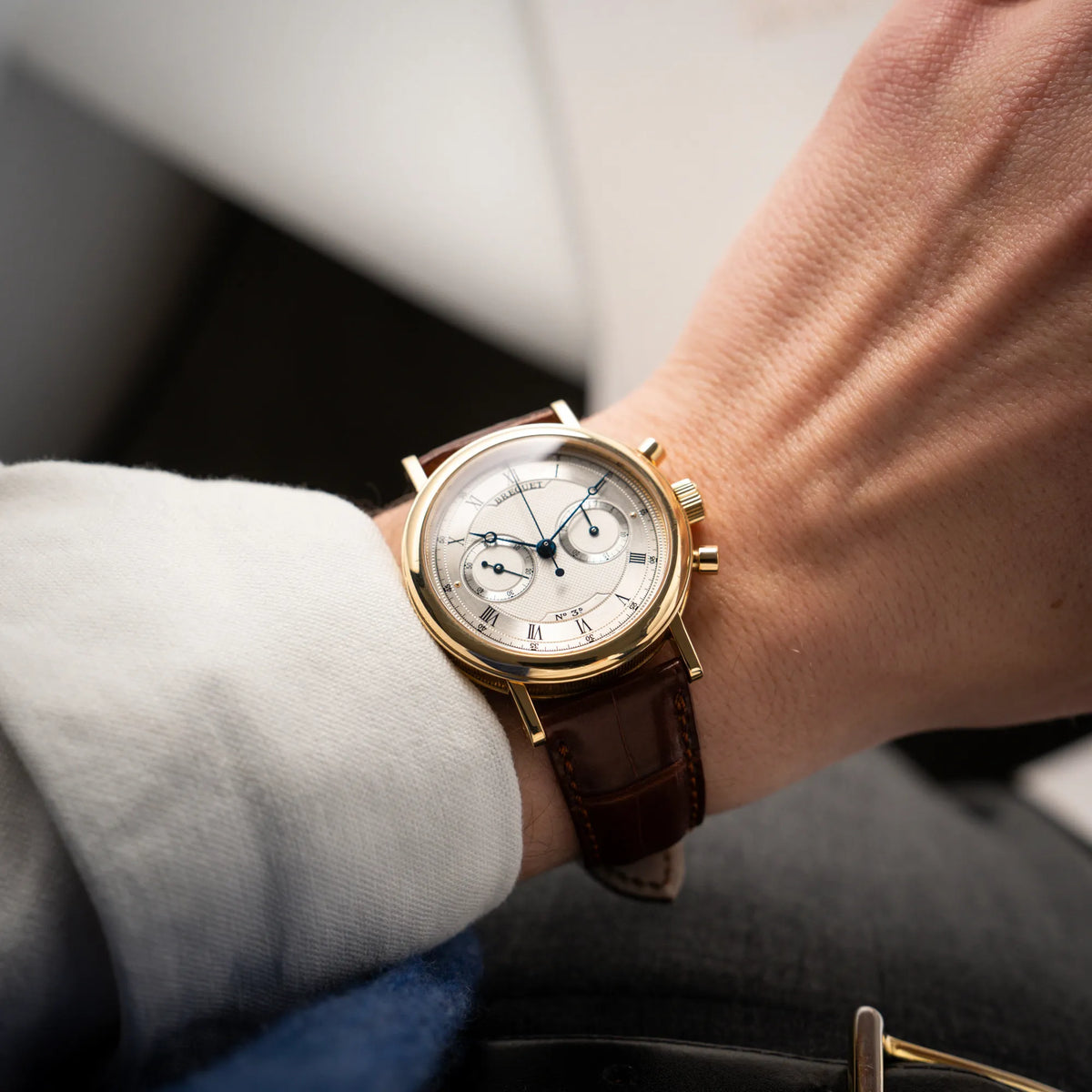 Mann trägt die Breguet Classique Chronograph der Referenz 5237 in Gelbgold mit silbernem guillochiertem Zifferblatt am braunem Lederband  an seinem Handgelenk