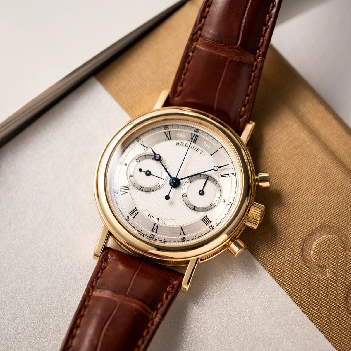 Produktfotografie als Titelbild für den Breguet Classique Chronograph der Referenz 5237 in Gelbgold mit silbernem guillochiertem Zifferblatt am braunem Lederband 
