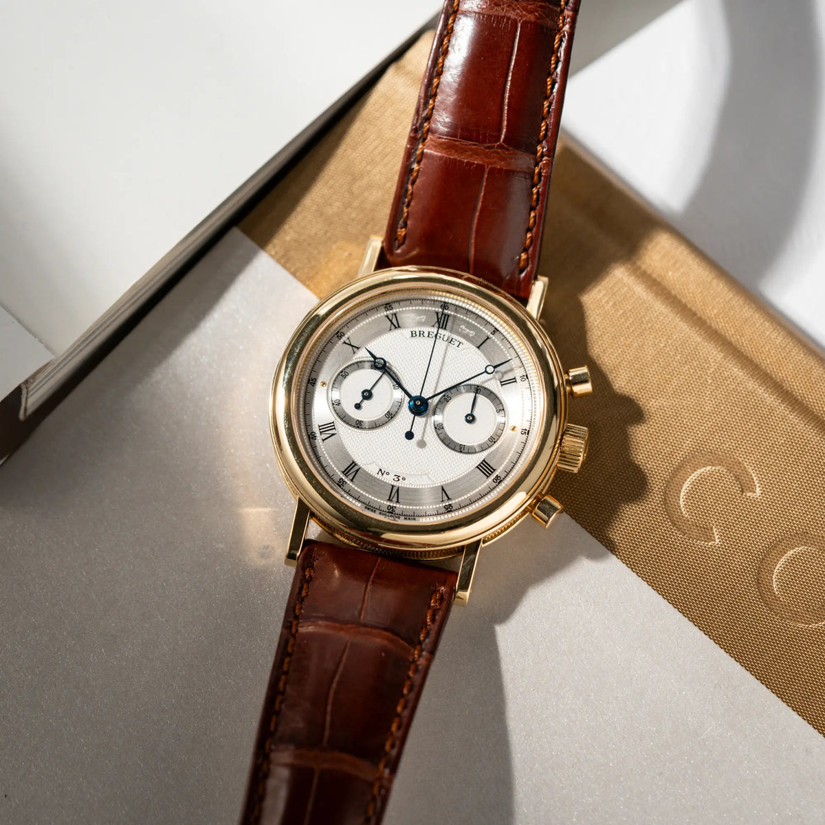 Produktfotografie der Breguet Classique Chronograph der Referenz 5237 in Gelbgold mit silbernem guillochiertem Zifferblatt am braunem Lederband 