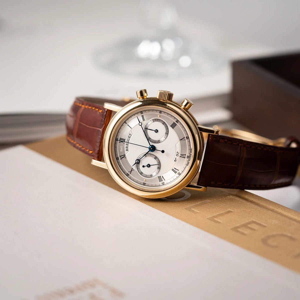 Breguet Classique Chronograph der Referenz 5237 in Gelbgold mit silbernem guillochiertem Zifferblatt am braunem Lederband  liegt auf der seitlichen Gehäuseflanke
