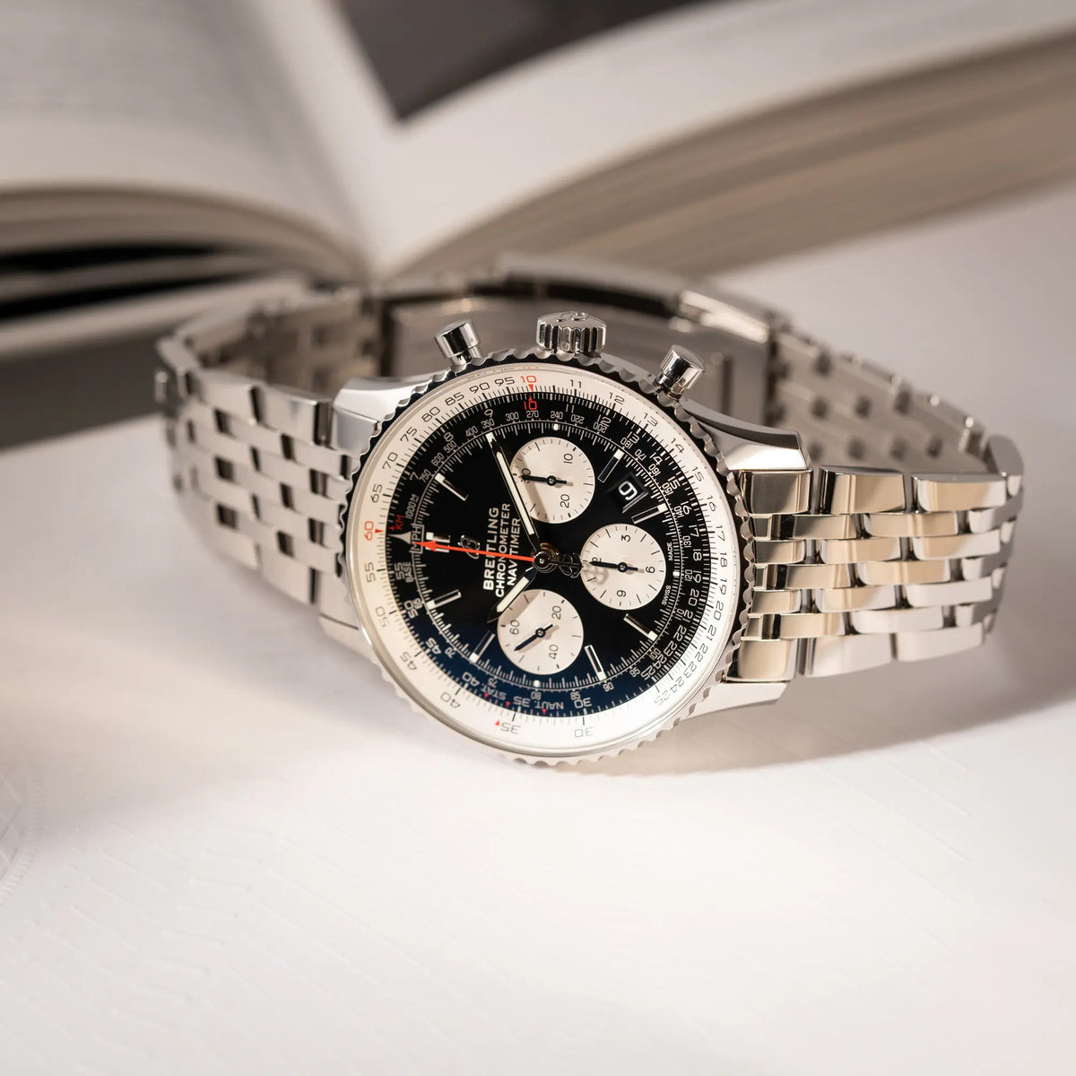 Produktfotografie der Breitling Navitimer B01 Chronograph der Referenz AB0121211B1A1 mit Reverse-Panda Zifferblatt in schwarz mit weißen Hilfszifferblätter, während die Uhr auf dem Gehäuse liegt