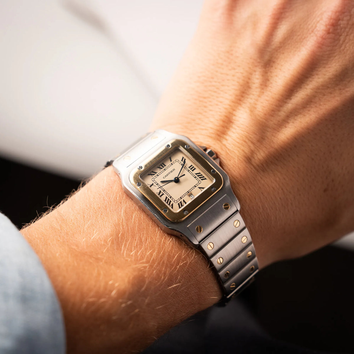 Mann trägt die Cartier Santos Galbee BiColor der Referenz 187901 mit Stahl-Gold-Gehäuse am Stahlband  mit dem Cartier-typischen Schrauben, die ebenfalls in Gelbgold gehalten sind, und einem cremfarbenen Zifferblatt mit klassischen römischen Indizes an seinem Handgelenk