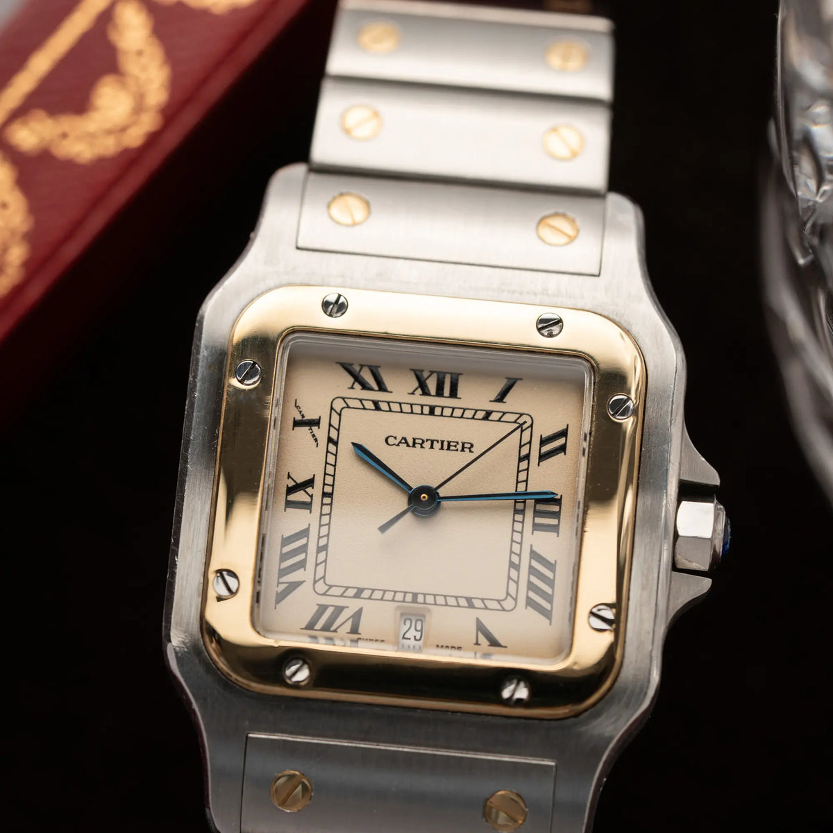 Produktfotografie zeigt den Uhrenkopf der Cartier Santos Galbee BiColor der Referenz 187901 mit Stahl-Gold-Gehäuse am Stahlband  mit dem Cartier-typischen Schrauben, die ebenfalls in Gelbgold gehalten sind, und einem cremfarbenen Zifferblatt mit klassischen römischen Indizes