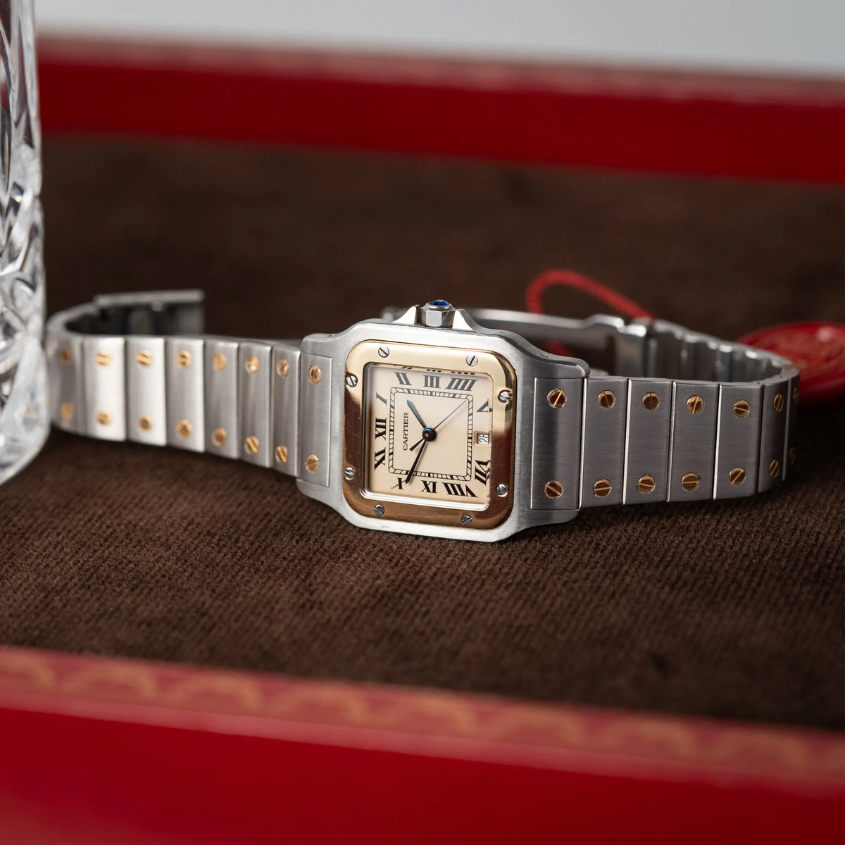 Produktfotografie der seitlich auf dem Uhrengehäuse liegenden Cartier Santos Galbee BiColor der Referenz 187901 mit Stahl-Gold-Gehäuse am Stahlband  mit dem Cartier-typischen Schrauben, die ebenfalls in Gelbgold gehalten sind, und einem cremfarbenen Zifferblatt mit klassischen römischen Indizes