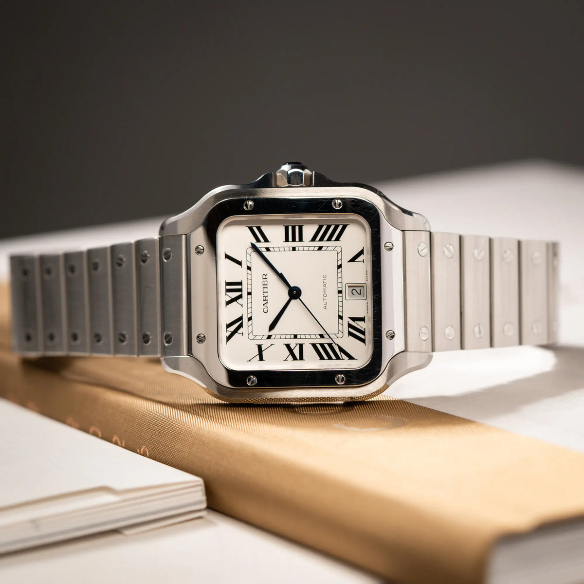 Produktfotografie der seitlich auf dem Gehäuse liegenden Cartier Santos de Cartier als großes Modell der Referenz WSA0018 mit dem klassischen weißen Zifferblatt und römischen Indizes zeigt die Uhr mit den polierten und satinierten Oberflächen
