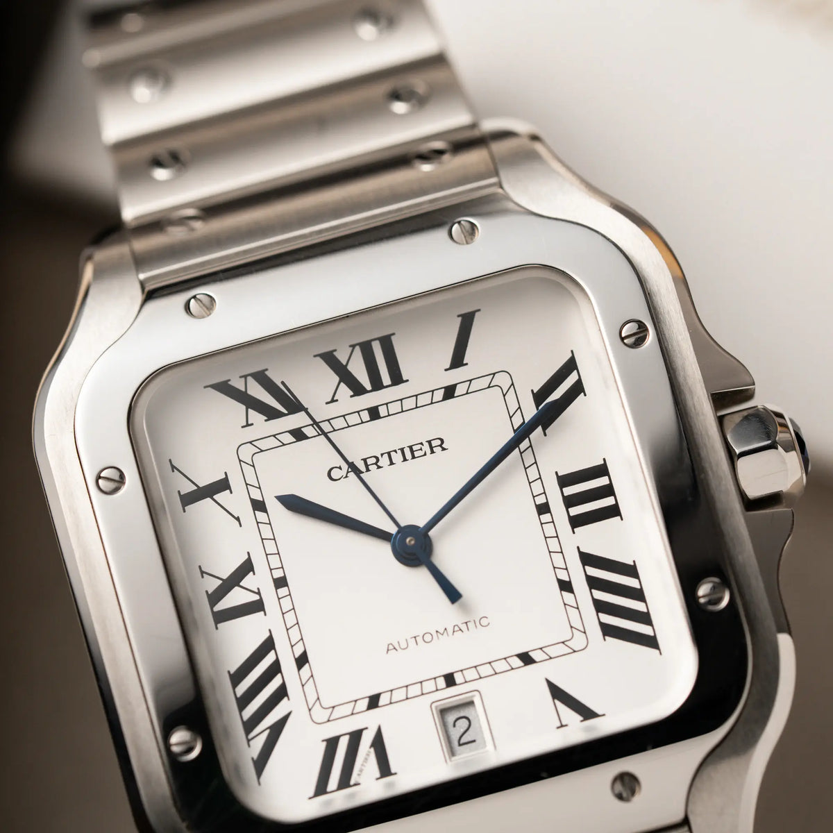 Makroaufnahme der Cartier Santos de Cartier als großes Modell der Referenz WSA0018 mit dem klassischen weißen Zifferblatt und römischen Indizes zeigt den Uhrenkopf mit dem polierten Lünetten-Aufsatz und satinierten Oberflächen