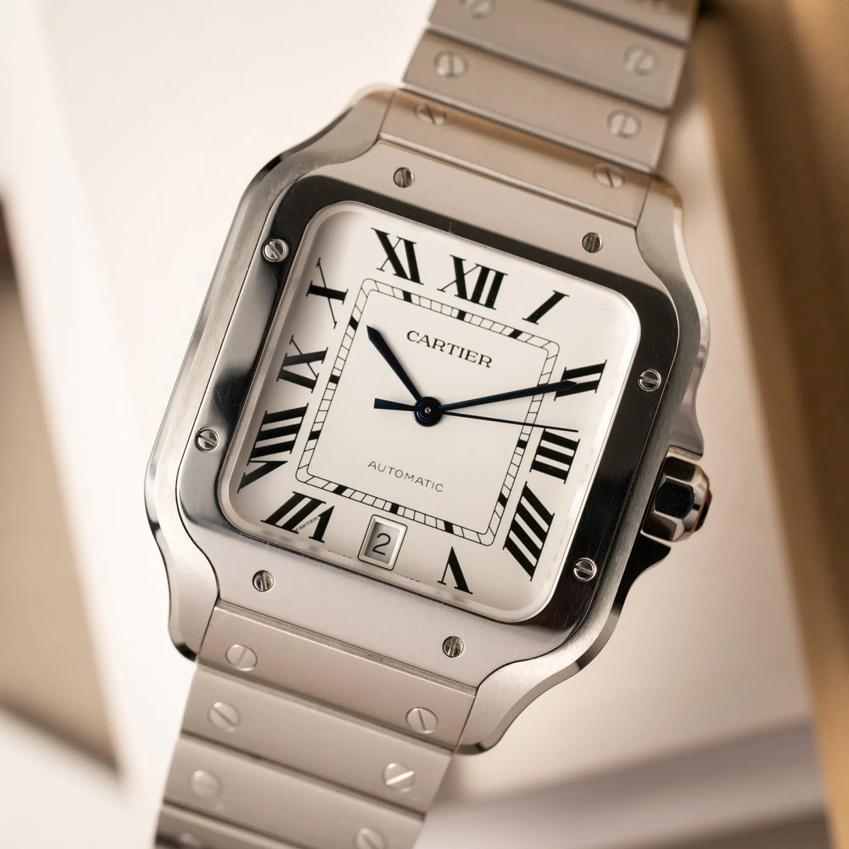 Detailaufnahme der Cartier Santos de Cartier als großes Modell der Referenz WSA0018 mit dem klassischen weißen Zifferblatt und römischen Indizes und einem Datumsfenster bei 6 Uhr zeigt die Uhr mit den polierten und satinierten Oberflächen