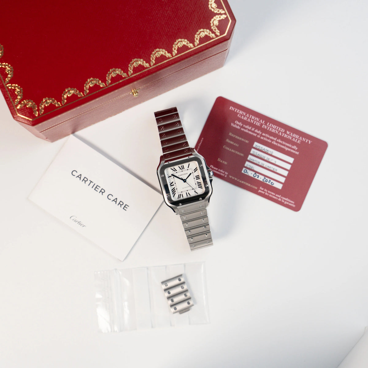 Produktfotografie der Cartier Santos Medium mit dem klassischen weißen Zifferblatt mit römischen Indizes zusammen mit dem Lieferumfang