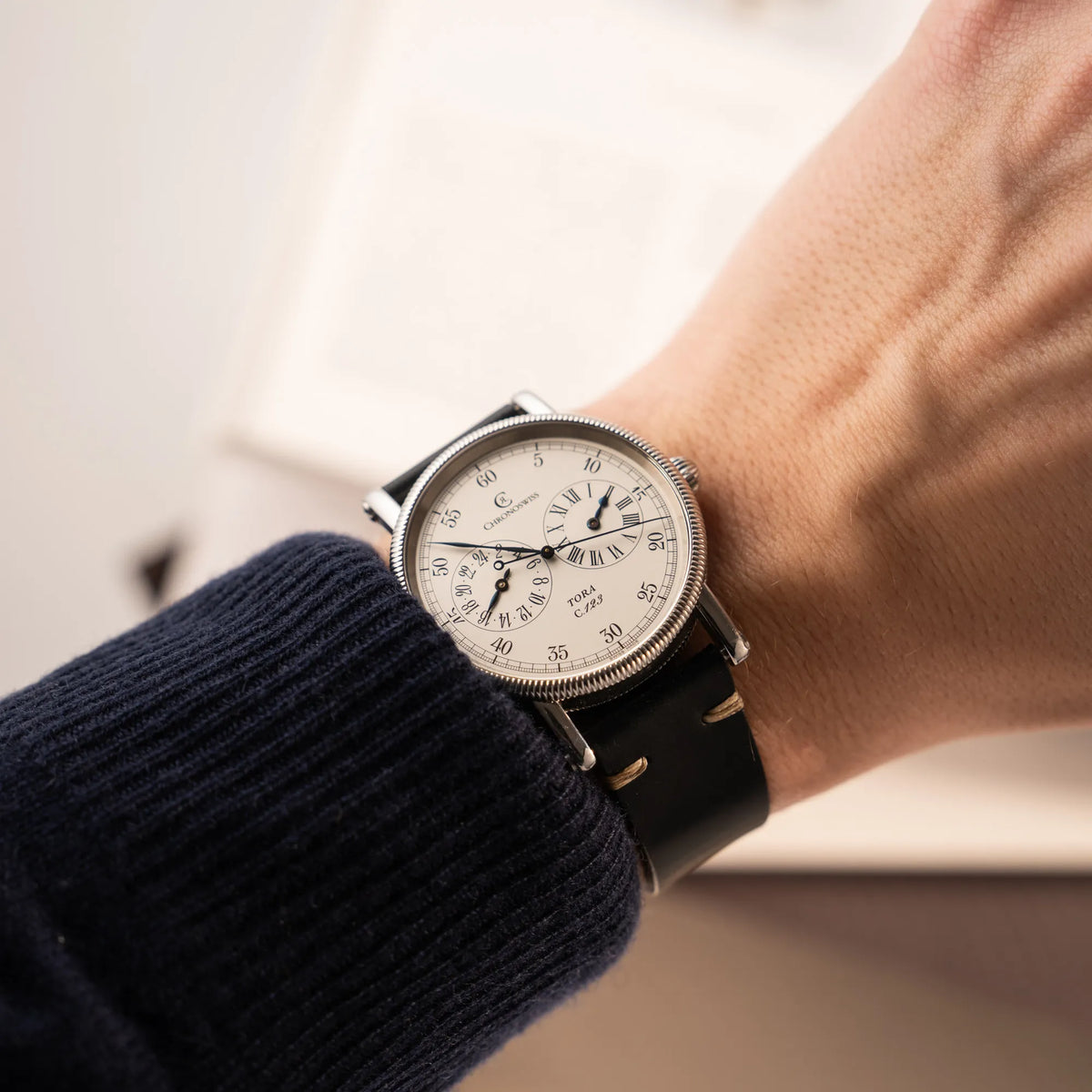 Wristshot it der Chronoswiss Regulator Tora C123 mit weißem Zifferblatt mit zwei symmetrisch angeordneten Hilfszifferblättern mit römischen Indizes an einem Männerhandgelenk