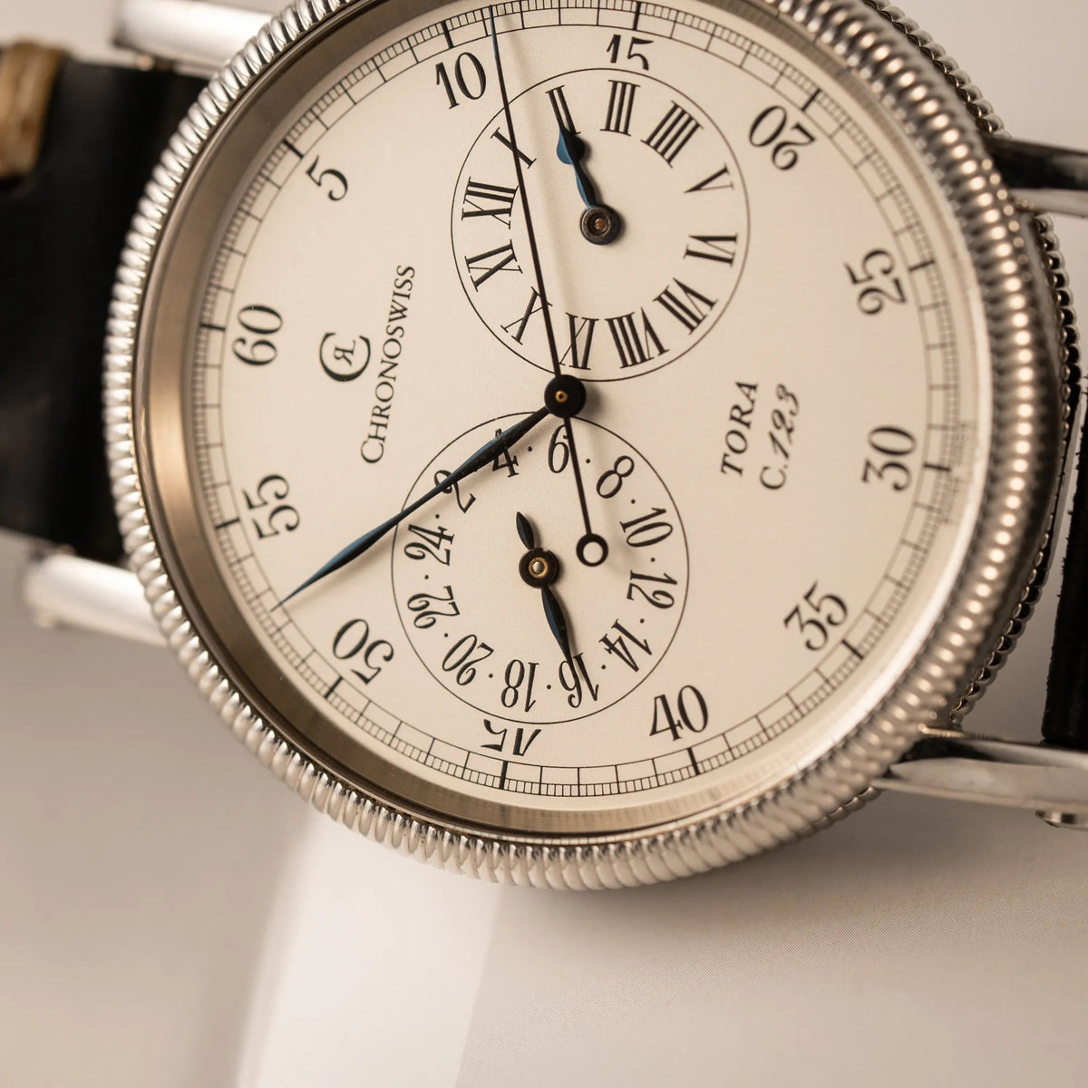 Detailaufnahme der seitlich auf dem Gehäuse liegenden Chronoswiss Regulator Tora C123 mit weißem Zifferblatt mit zwei symmetrisch angeordneten Hilfszifferblättern mit römischen Indizes