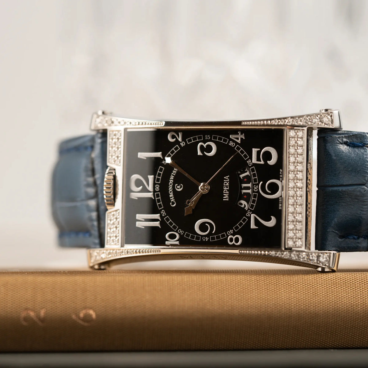 Detailaufnahme der Chronoswiss Imperia Constanze mit diamantbesetzten-Stahlgehäuse mit schwarzem Zifferblatt an einem petrol-blauem Lederband