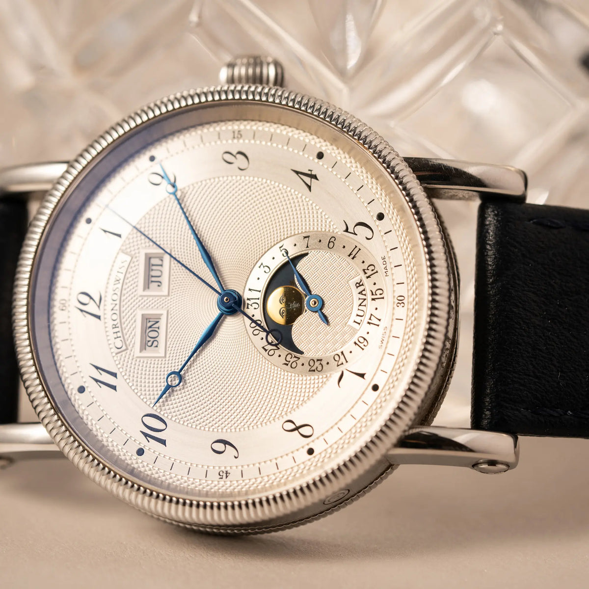 Produktfotografie der seitlich auf dem Gehäuse liegenden Chronoswiss Klassic Luna Mondphase CH9323 mit silbernem, guillochiertem Zifferblatt mit Kalenderanzeige auf 12 Uhr und einer Mondphase-Anzeige bei 6 Uhr