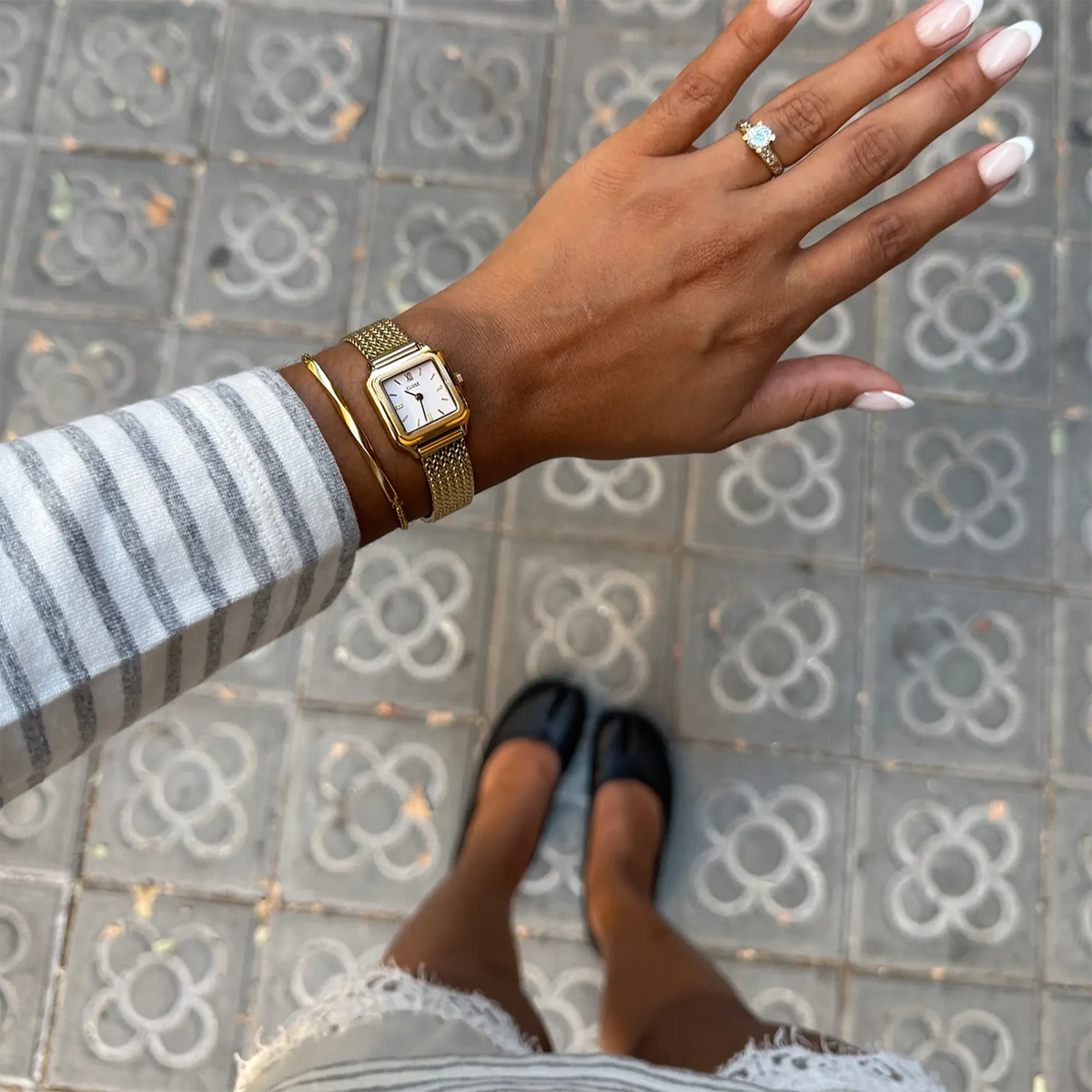 Lifestylebild mit der goldfarbenen Cluse Gracieuse Mini Damenuhr CW15509  mit weißem Zifferblatt am Mesh-Armband am Handgelenk einer jungen Dame