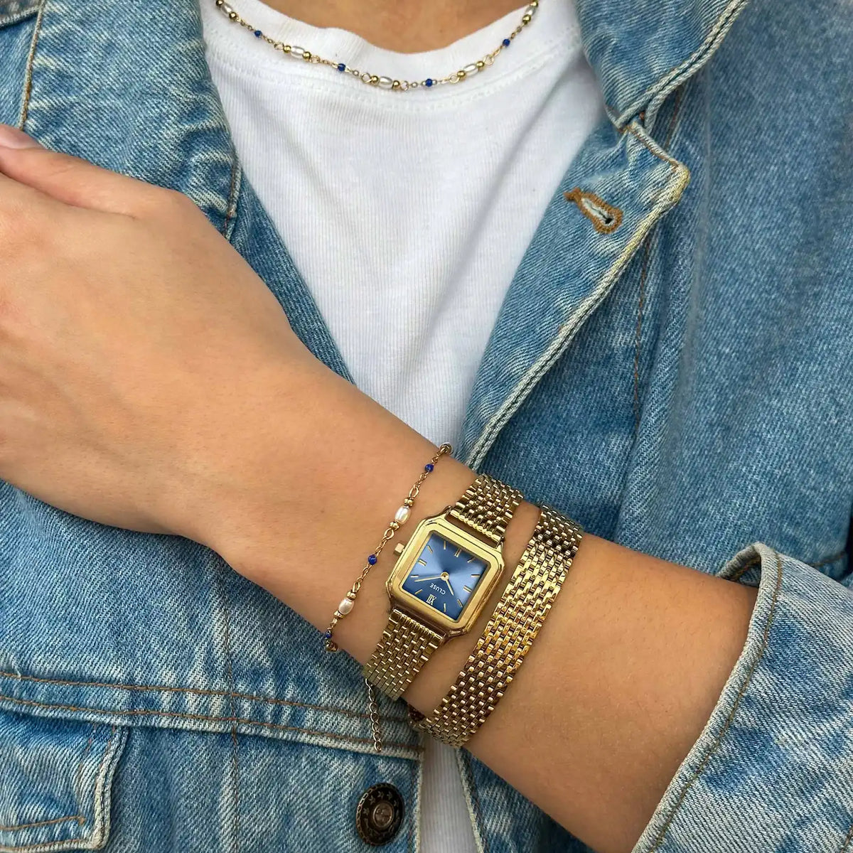 Frau trägt die der goldfarbenen Cluse Gracieuse Petite Damenuhr mit rechteckigem Gehäuse und blauem Zifferblatt an einem feingliedrigen Doppel-Armband an ihrem Handgelenk
