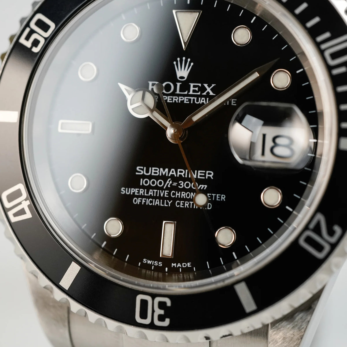 Makroaufnahme des Zifferblatts der Rolex Submariner Date in schwarz, Referenz 16610, mit Flat-Four-Lünette
