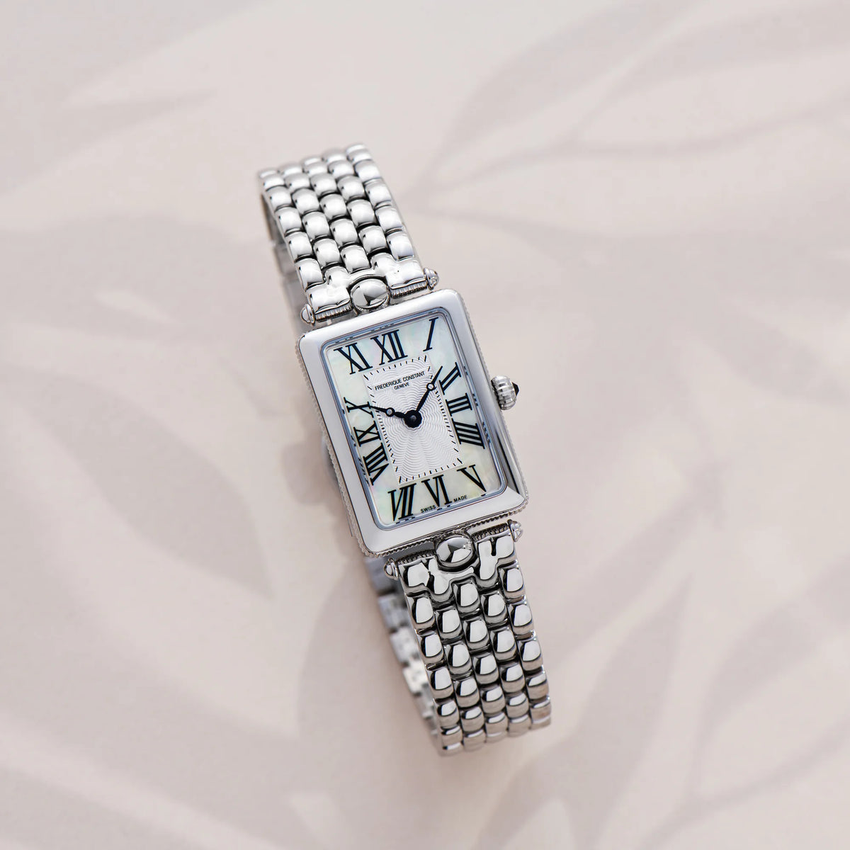 Produktfotografie der Frederique Constant Art Deco Carre aus der Classics Kollektion mit einem rechteckigen Uhrengehäuse mit einem Zifferblatt in Perlmutt-Optik und schwarzen, römischen Ziffern auf einem beigen Hintergrund
